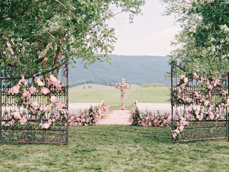 outdoor wedding ceremony venue with iron gates and cross decorated in pink roses
