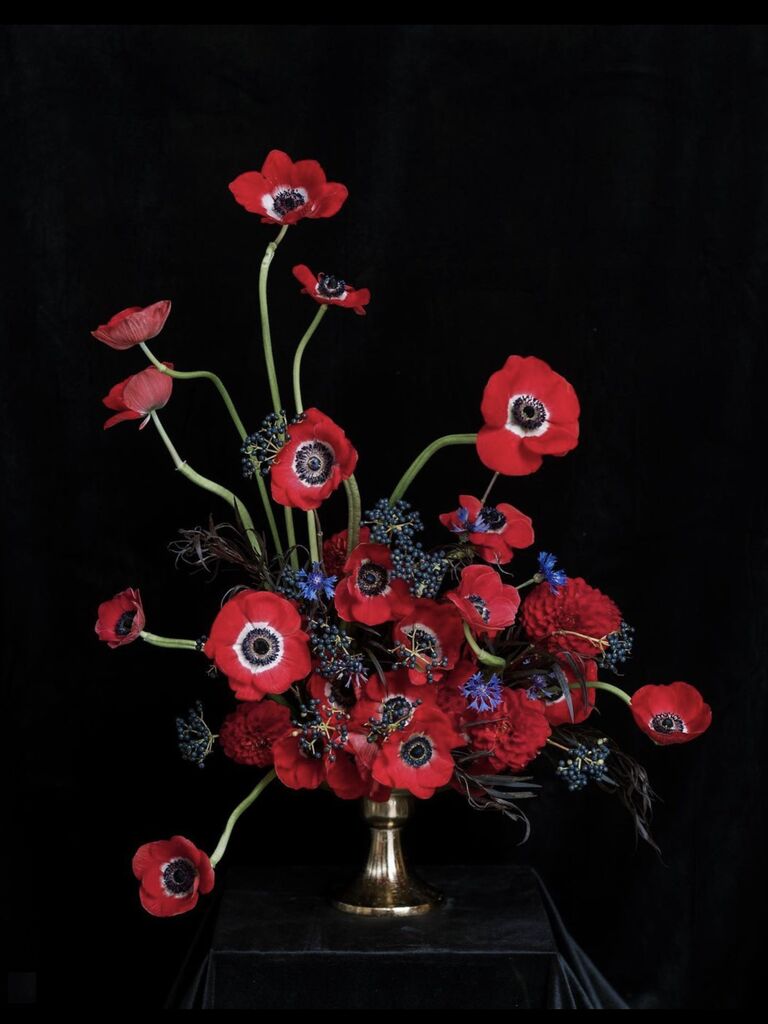 modern wedding centerpiece with red anemones in gold compote vase against a black backdrop