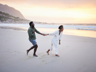Couple holding hands walking on beach at engagement moon
