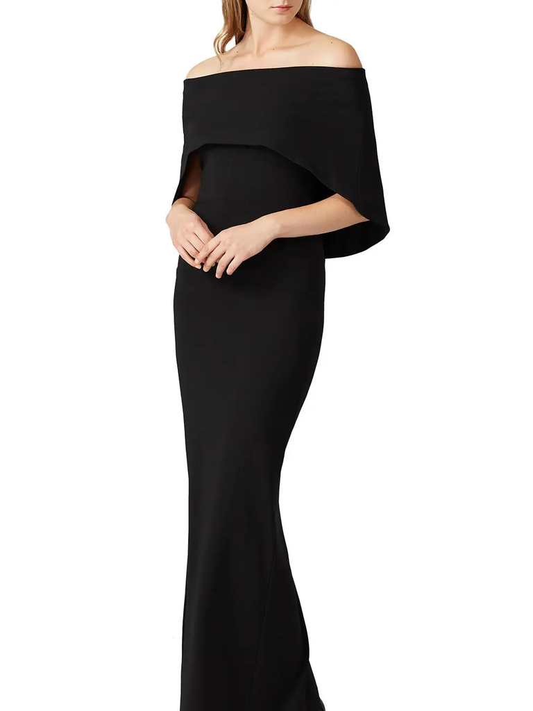 A model wears this off-the-shoulder black mother of the bride dress with cape.