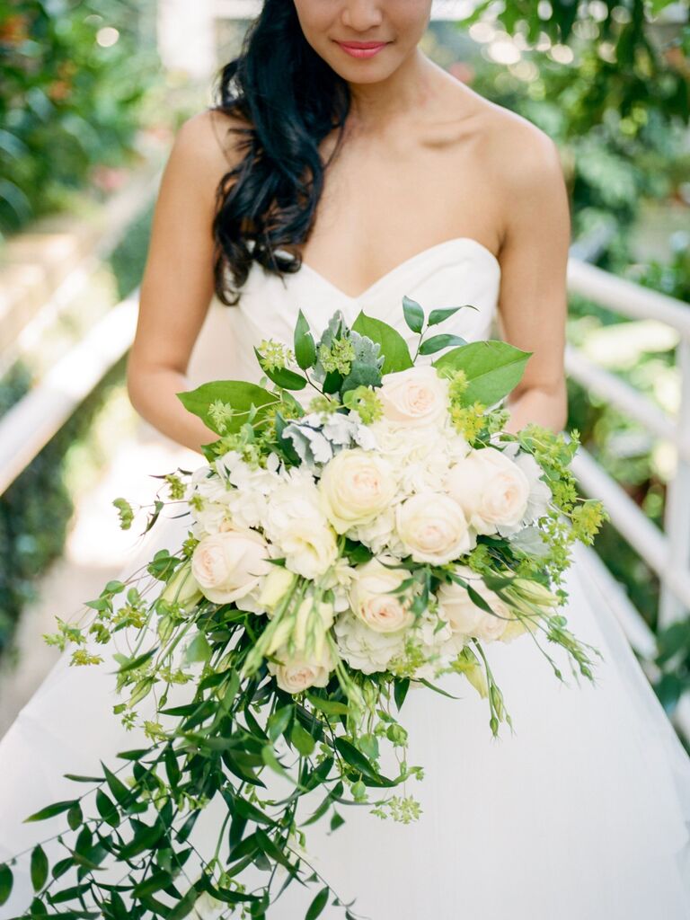 bride holds cascading wedding bouquet with white roses and greenery