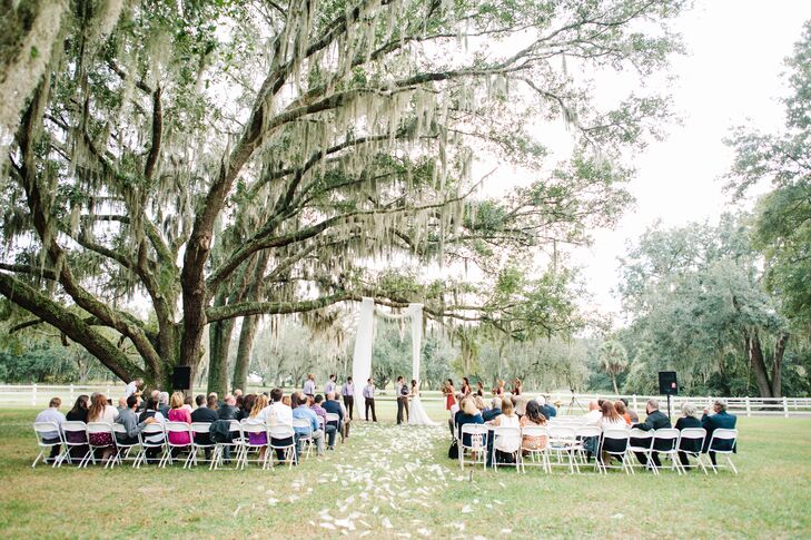 Wanting to highlight their venue, Shelby and Zack kept to almost all-white decor. Their guests sat in rows of white folding chairs accented by tons of classic, ivory skeleton magnolia leaves scattered over the aisle. Their wedding arch was even made with ivory fabric draped across a nearby oak tree.