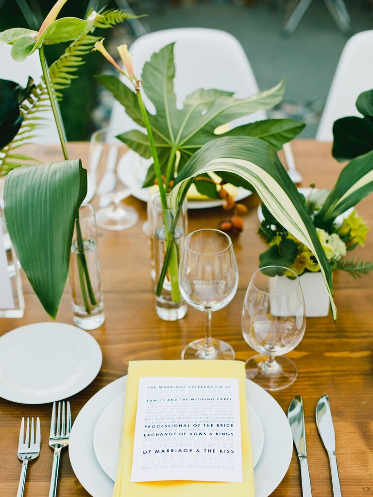 tropical wedding centerpiece with banana leaves and greenery in bud vases
