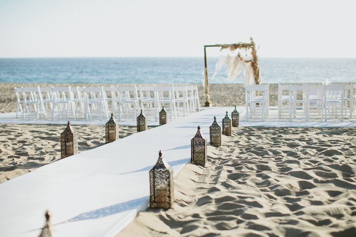 A sturdy white platform aisle lined with lanterns led to the dream catcher wedding arch where Gwynne and David exchanged vows. "I wanted a boho beach wedding with rich orange sunset colors in the flowers,” Gwynne says. “The Sunset Restaurant was the perfect location because we were able to have our ceremony right on the beach at sunset.”