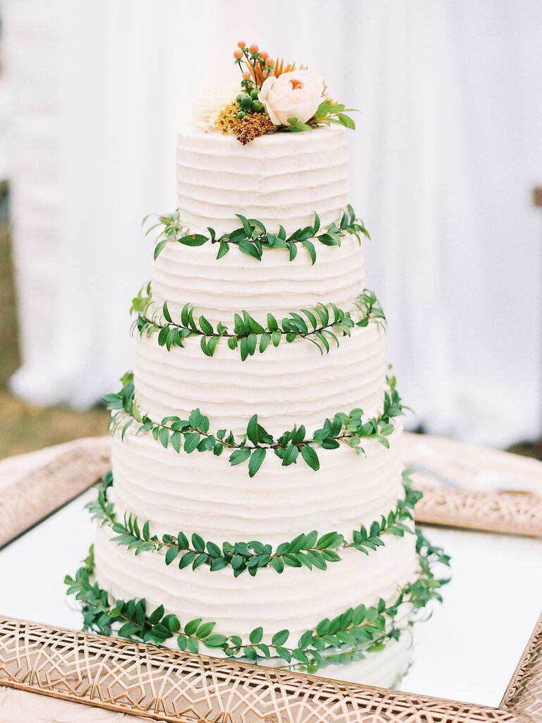 five-tier white buttercream wedding cake with greenery in between each tier and light pink rose on top