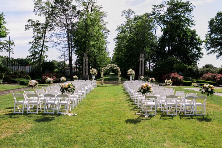 The ceremony took place on the Guggenheim Mansion’s great lawn, overlooking rows of lush trees at the Village Club of Sands Point in Sands Point, New York. Noel and Tim exchanged heartfelt vows under a wrought iron wedding arch decorated with wispy vines, greenery and full peach, cream and coral garden roses, hydrangeas and more. Large stone urns lined the aisles, bursting with berries, stock, amaranths, hydrangeas and roses.