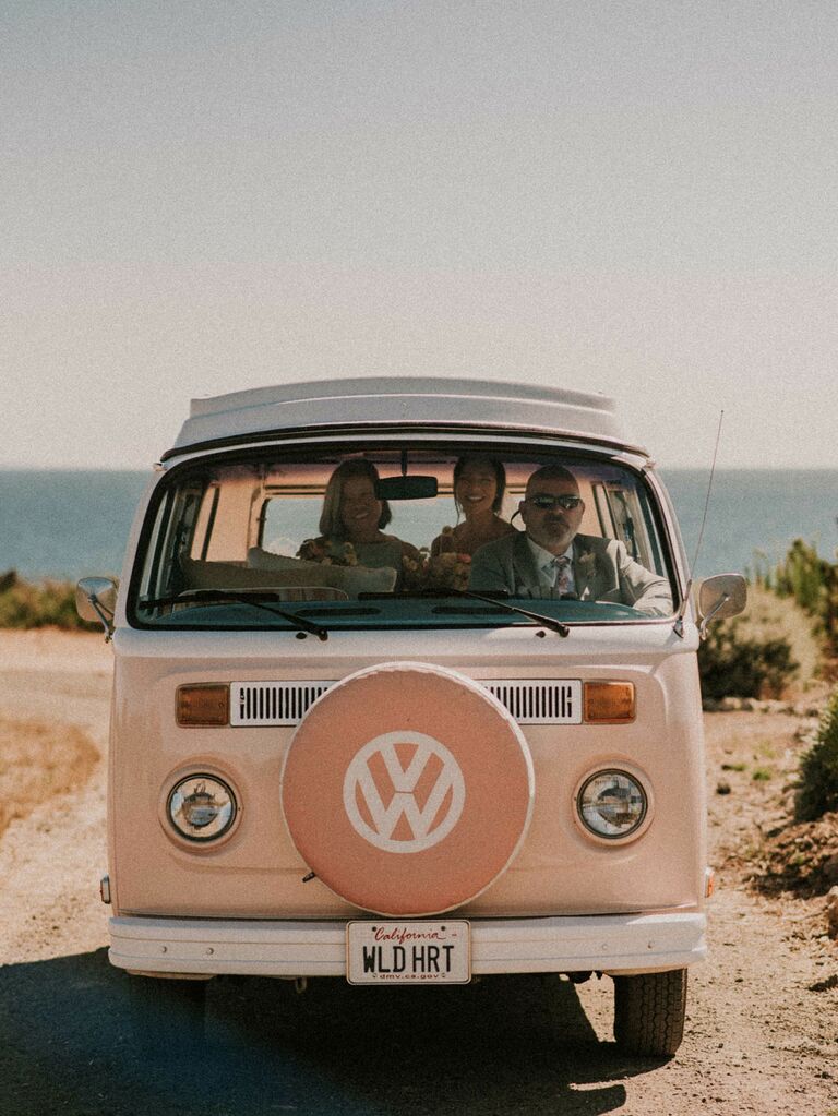Bride and groom in vintage pink Volkswagen getaway car at boho wedding