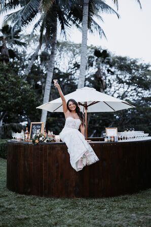 Bride Sits on Top of Outdoor Bar at Hawaii Wedding, Poses With Couple Glass