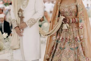 Sikh Groom in White Achkin Outfit With Sword, Bride in Colorful Lengha With Intricate Details Holding Groom's Palla