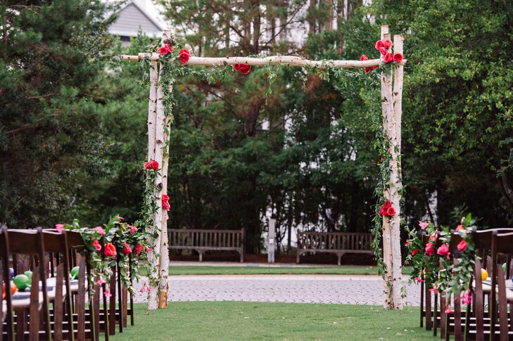 Their wedding arch captured the natural setting at St. Augustine Green with an understated design. Events by Nouveau, the couple's florist, decorated each birch-wood post with a grand garland of greenery and bunches of fuchsia garden roses, which also accented the aisle.