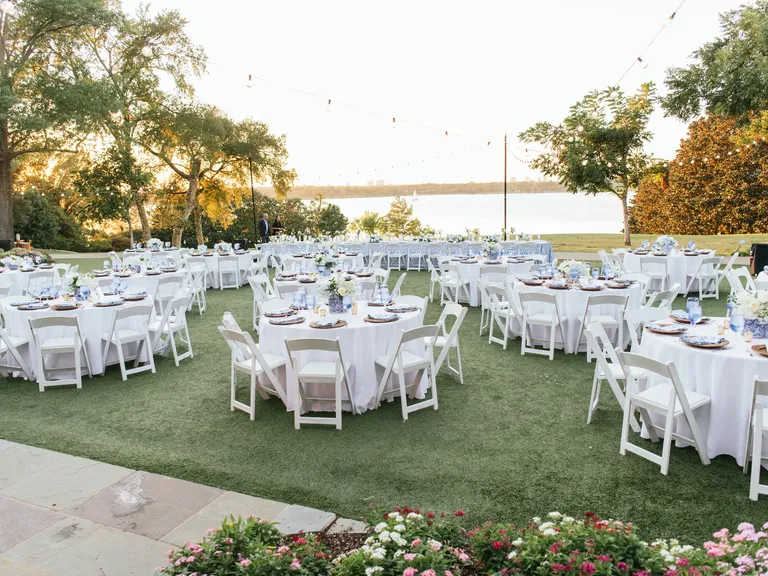 Outdoor reception space with white tables and chairs by the water at Dallas Arboretum wedding venue in Dallas, Texas