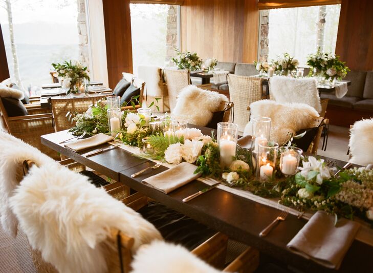 Rustic stone tables were pushed together to form one long table in the middle of the reception hall with green garlands running down the middle. Each table was decorated with candles, florals, and faux sheepskin placed on the backs of the seating.