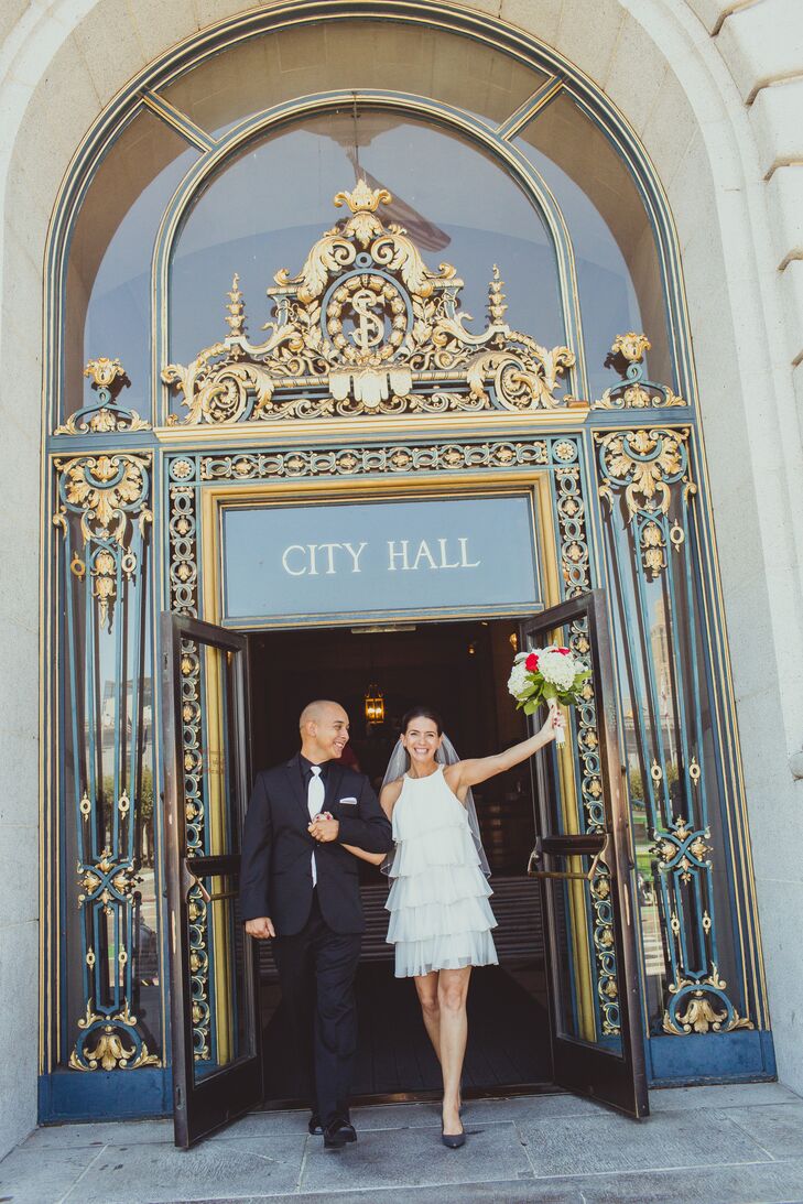 Tina and Erik exit through the elegant doors of the city hall venue as a married couple, with Tina holding up her ivory and red bouquet in the air.