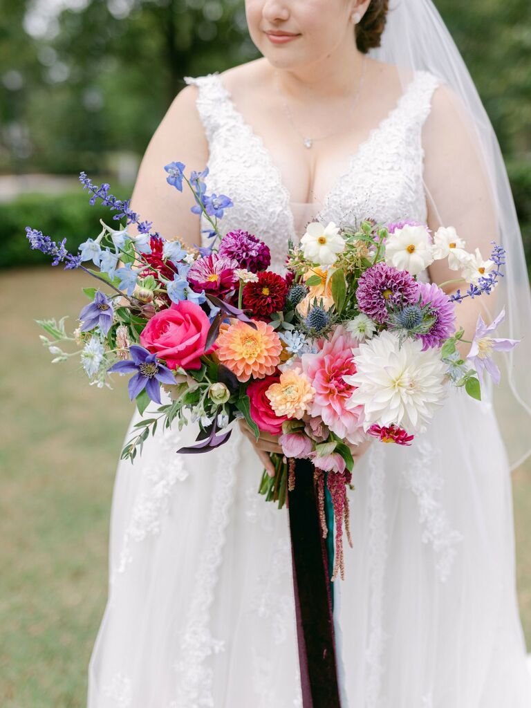 Bride holds a vibrant bouquet of colorful flowers, including purple dahlias. 
