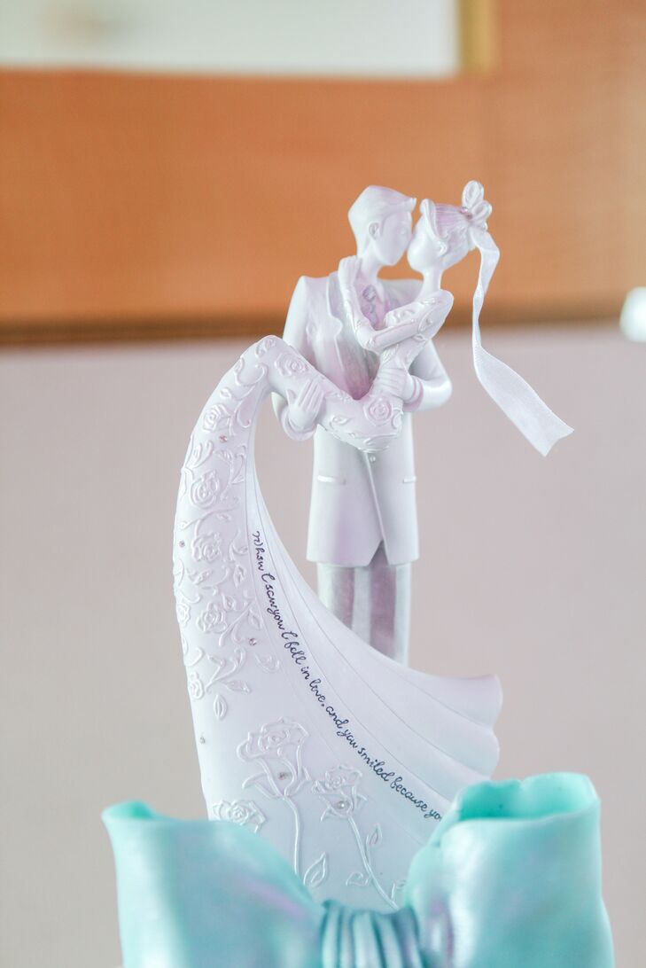 The couple’s whimsical white cake topper matched the crisp modern look of their wedding cake and reception. On the bride’s sweeping wedding dress train is a quote: “When I saw you I fell in love, and you smiled because you knew.”