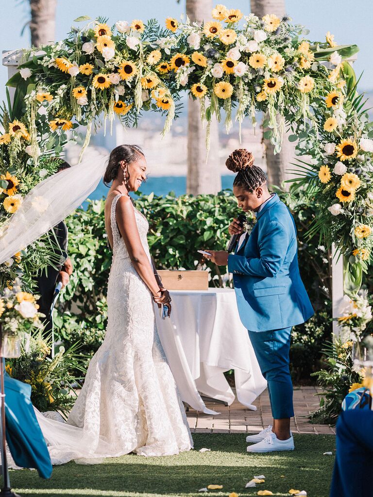 Brides exchanging vows in front of sunflower floral arch