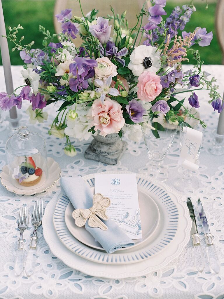 A pale pink and purple floral arrangement on a lace tablecloth at a wedding reception