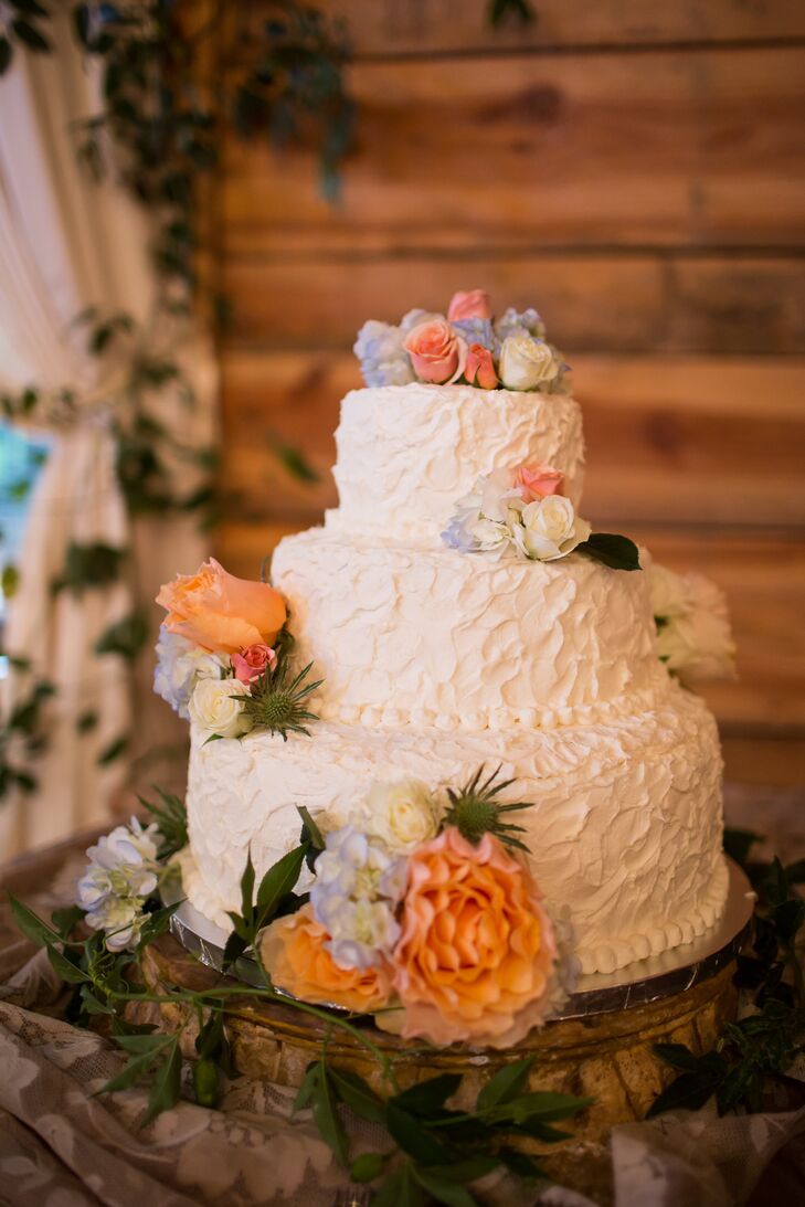 Cecelia's Cakes made Sarah and Nate's three-tier wedding cake, frosted in textured white buttercream. It had peach, blue and ivory flowers with touches of greens to match the colors throughout their Georgia wedding.