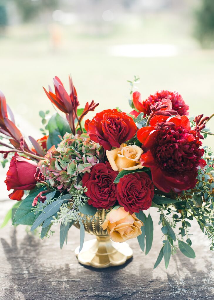 Red and pale orange roses accented with cascades of eucalyptus filled low gold vases for an elegant, autumnal look.