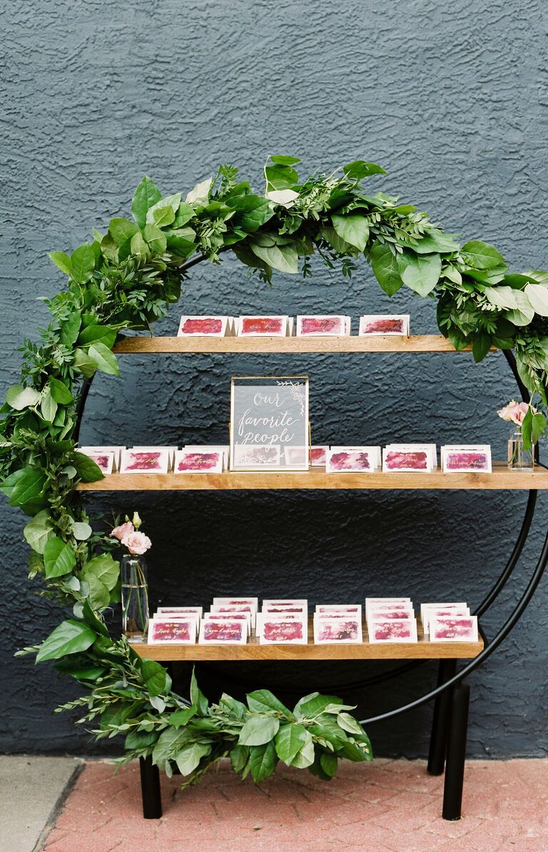 Escort card display with circular shelving unit covered in greenery