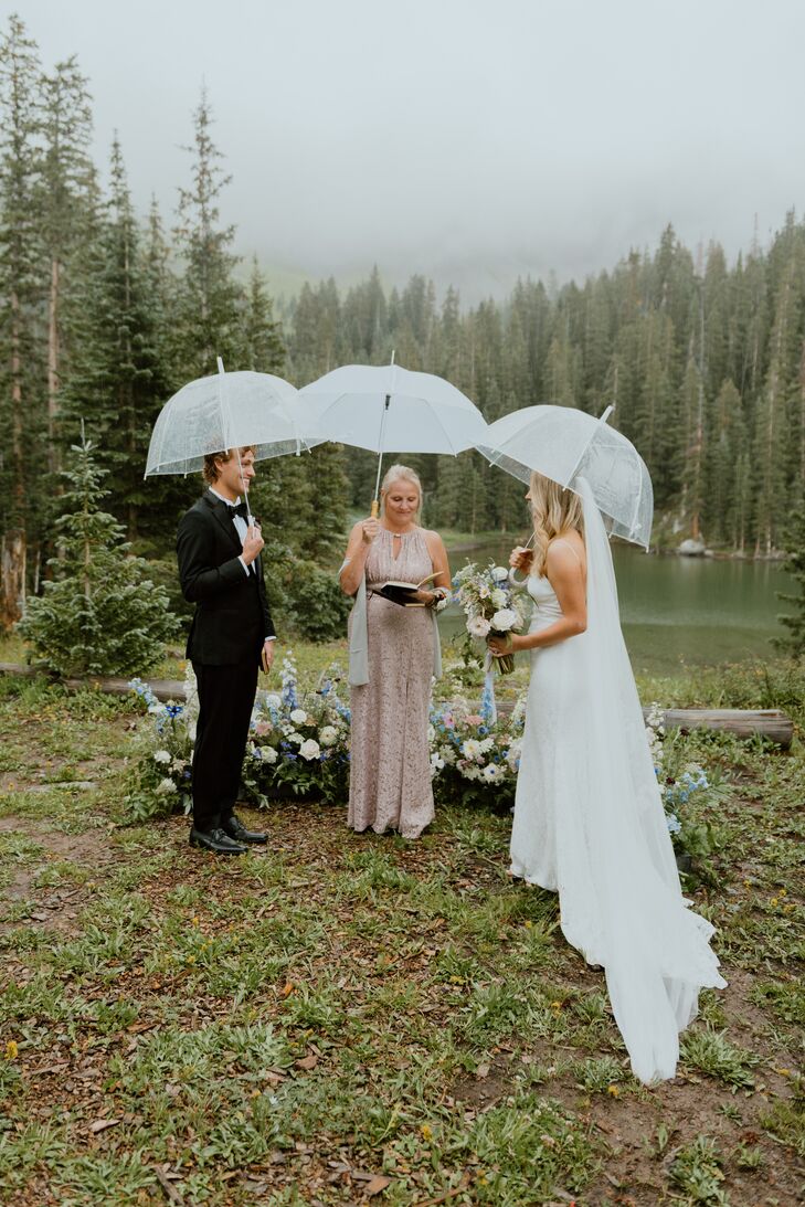 Groom, Bride and Officiant Holding Umbrellas at Rainy Mountain Ceremony With Floral Altar, Lakeside