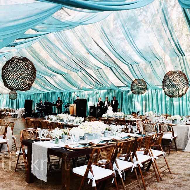 Dinner was served beneath a clear tent with transparent teal fabric draped from the ceiling, allowing guests to see the twinkling lights on the trees above. For a twist on chandeliers, wooden sticks were shaped into balls and hung overhead, with candles inside.