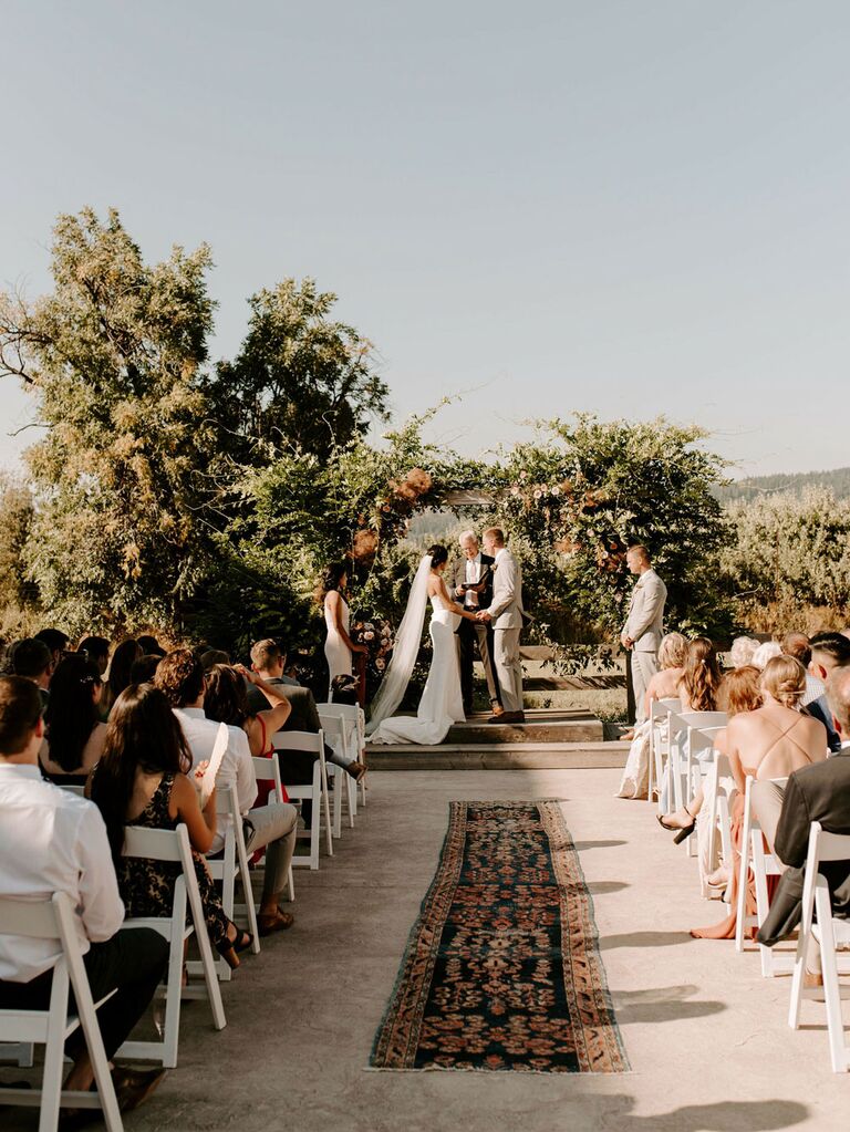 Bride and groom exchanging vows at bohemian wedding ceremony with printed rug covering aisle