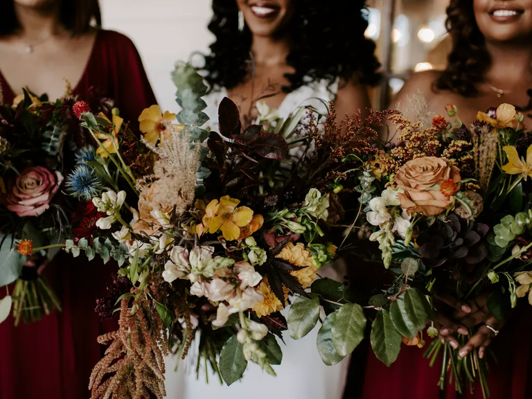 A bride and her bridesmaids smile for the camera, holding breathtaking autumnal bouquets.