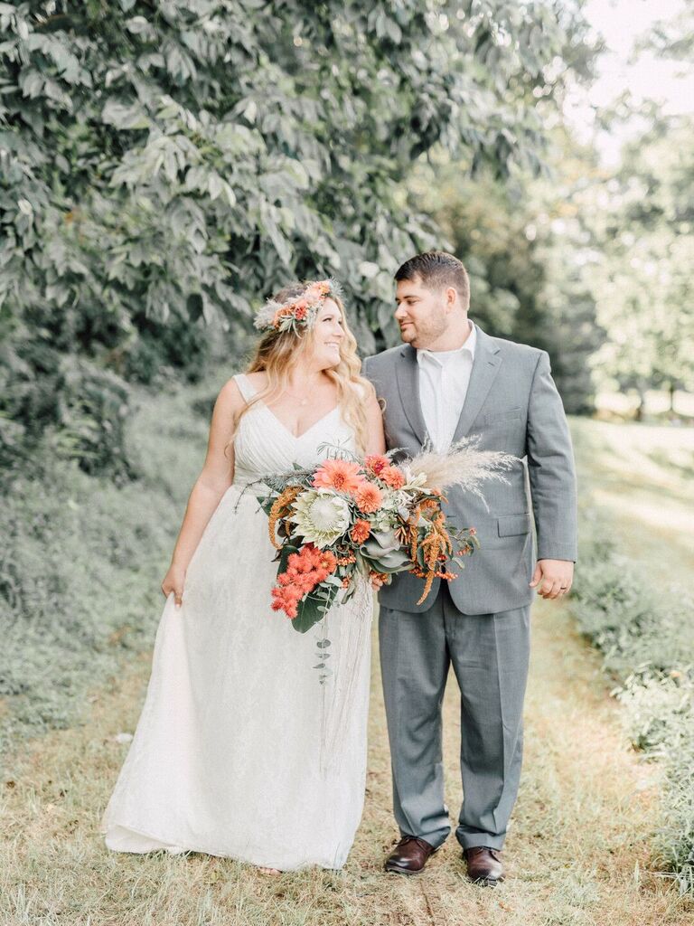 Couple looks at each other lovingly while holding a lush bouquet overflowing with dahlias and greenery. 