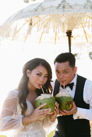 Bride and Groom Sip Out of Freshly Cut Coconuts Under Parasol at Hawaii Wedding