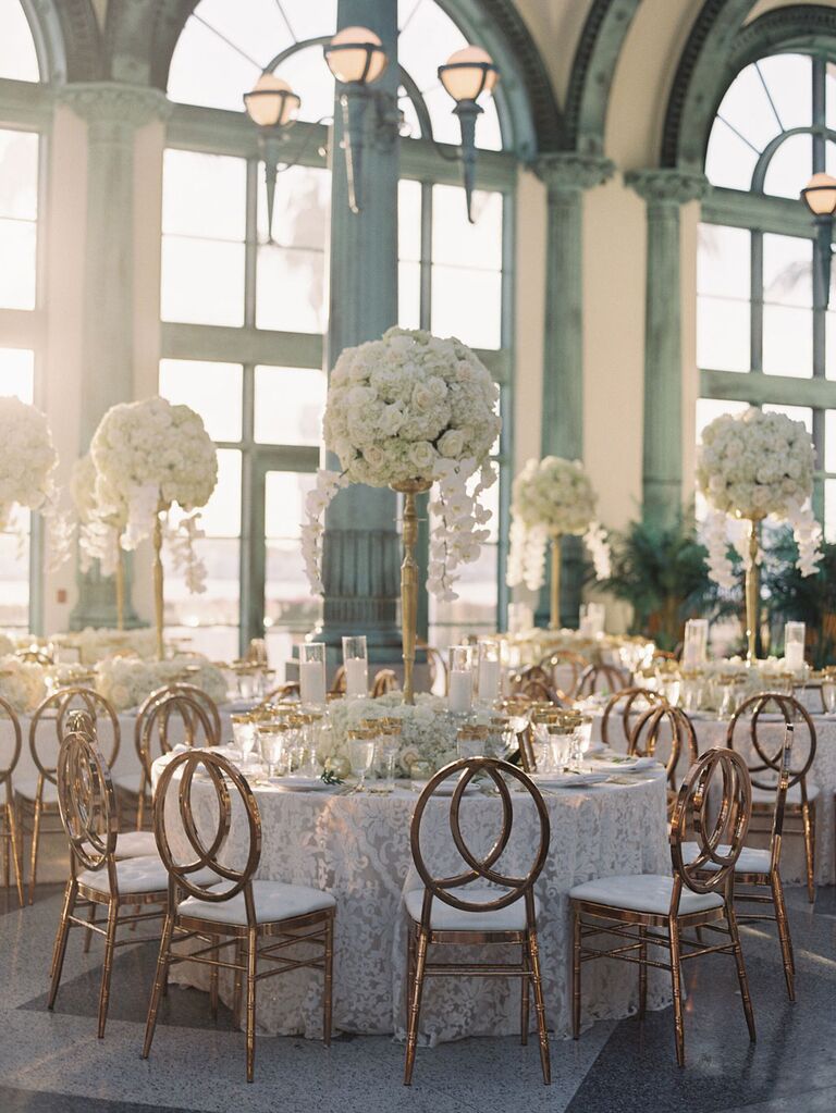 Opulent towering white floral center pieces at luxury wedding reception with gold chairs