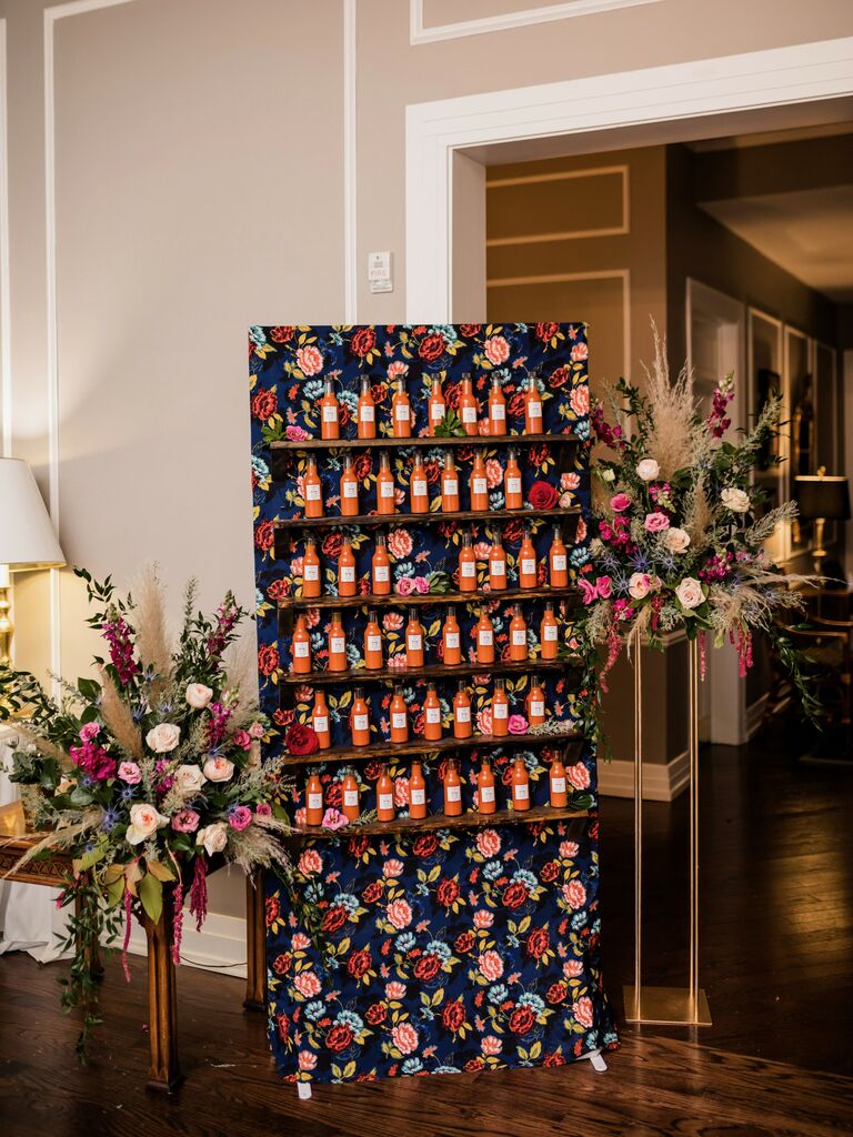 wedding favor display with hot sauce bottles on shelves against patterned floral fabric backdrop