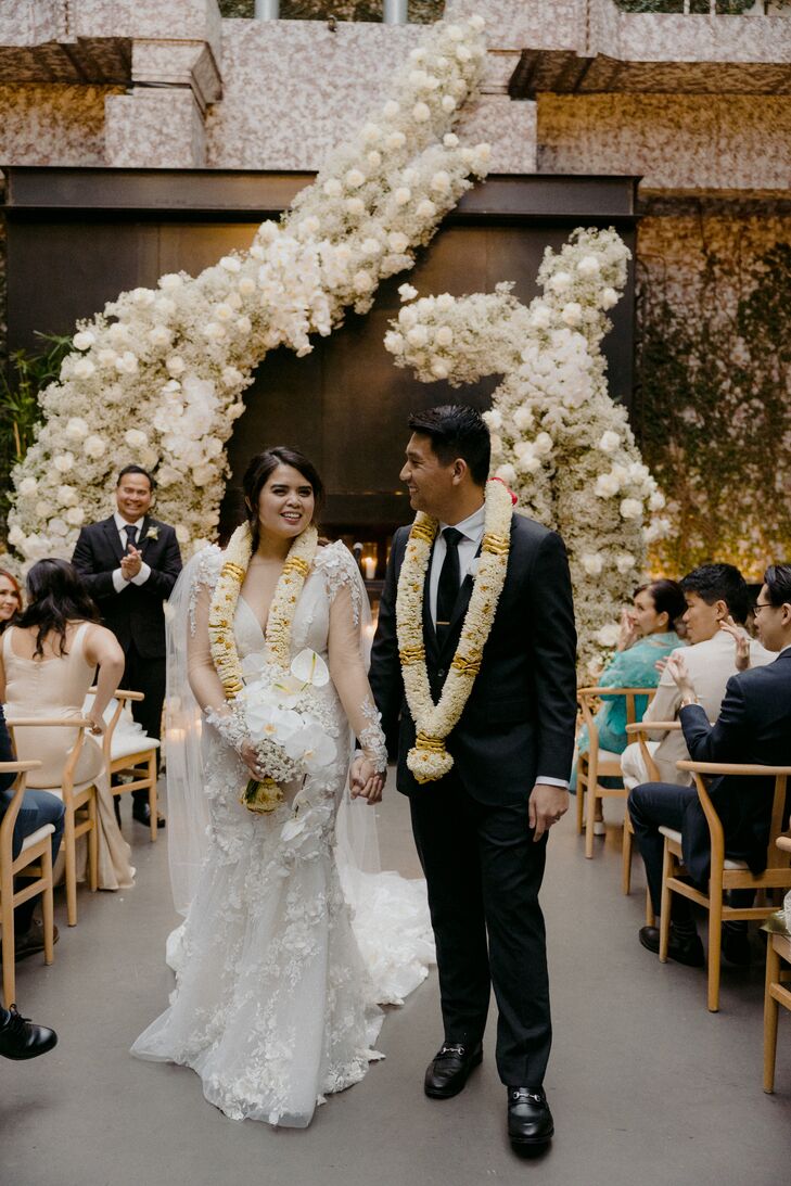 Bride and Groom Walk Up Aisle From Altar With Towering Floral Structure During Recessional, Leis