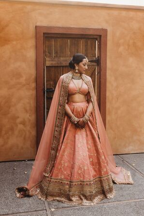 Bride in Two-Piece Lehenga in Rose Pink With Gold Designs, Earrings, Necklace