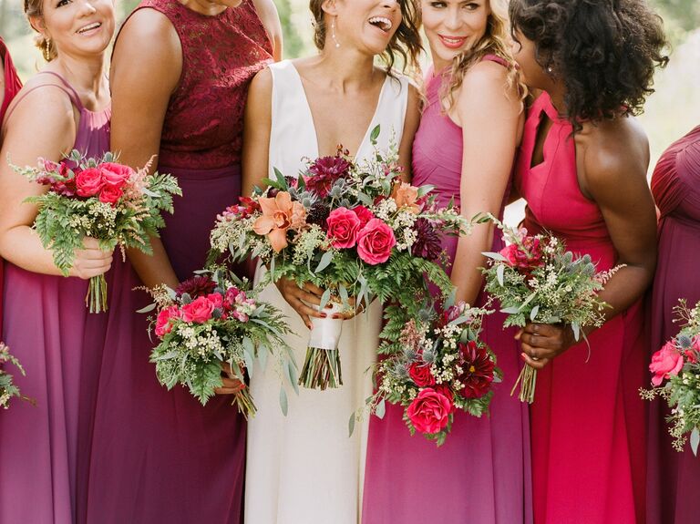 a bride stands with her bridesmaids carrying fall bouquets with fuchsia and orange flowers