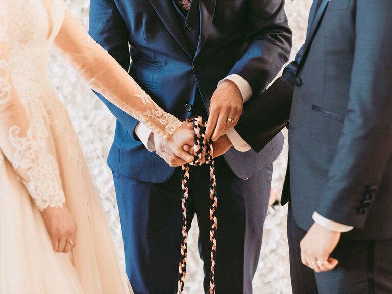 Bride and groom having hands tied with rope during traditional handfasting ceremony