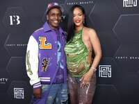 Singer Rihanna and boyfriend smile at the camera while walking a red carpet. 
