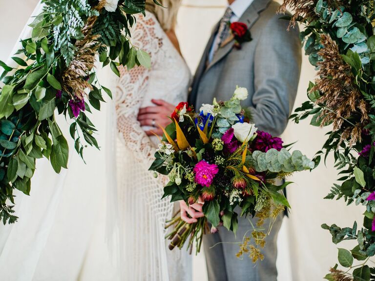 Bride and groom embrace while holding a vibrant bohemian bouquet. 