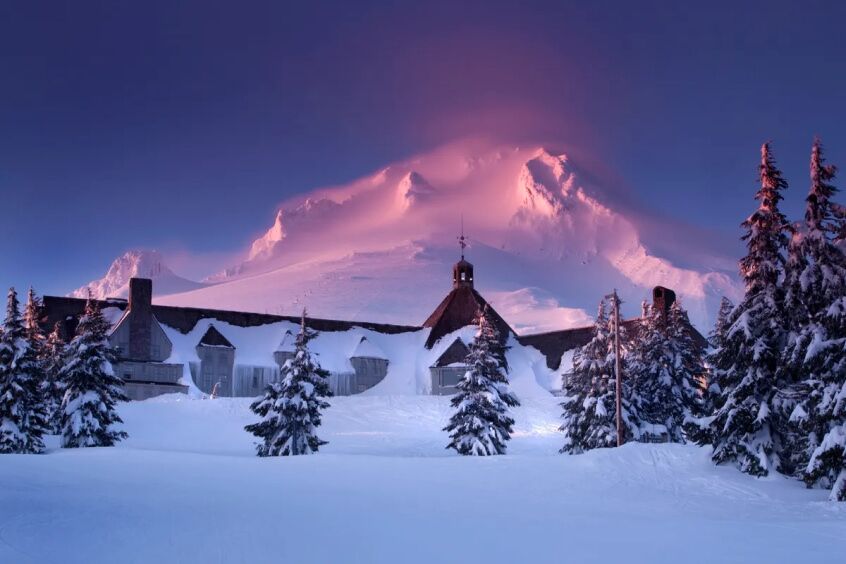 A scenic view of a snowy mountain with a rustic lodge in the background.