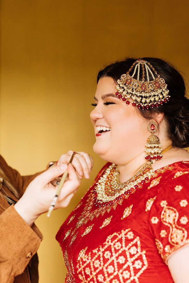 Bride in Red Lehenga and Ornate Jewelry Getting Makeup Done Before Ceremony