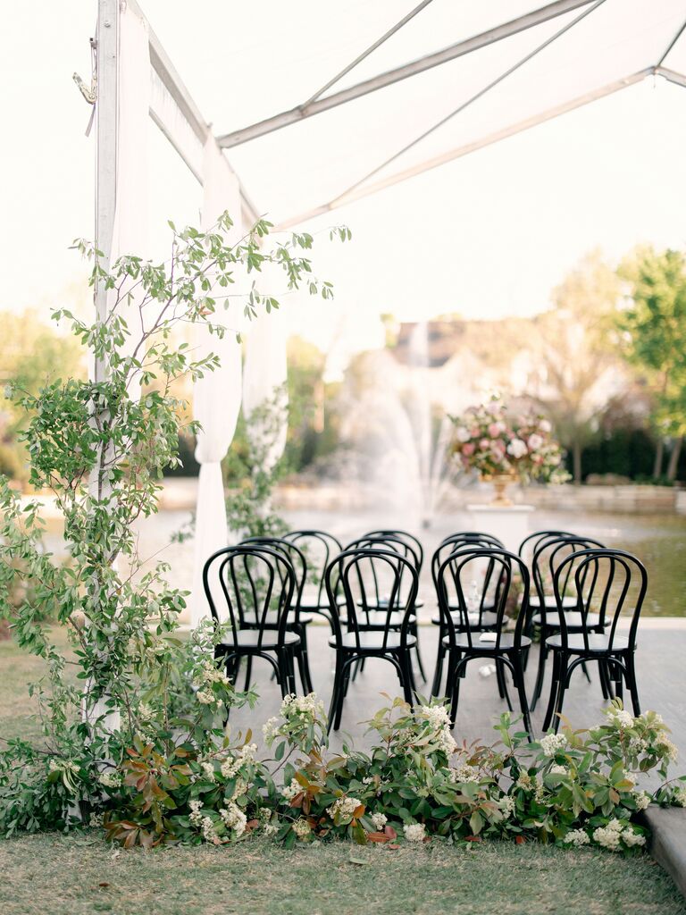 example of 2022 wedding color trend outdoor wedding ceremony under clear tent with greenery installation and black bistro chairs