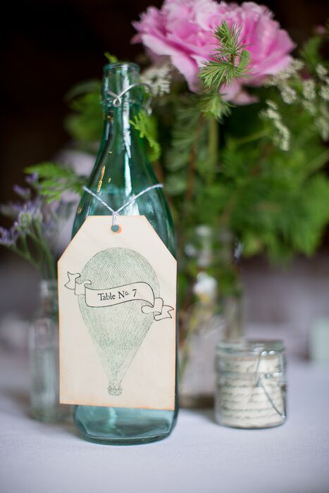 Gift tags with illustrations of hot air balloons hung from glass bottles for the vintage inspired table numbers.