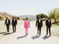 groom & groomsmen in pink and black suits walking near outdoor venue