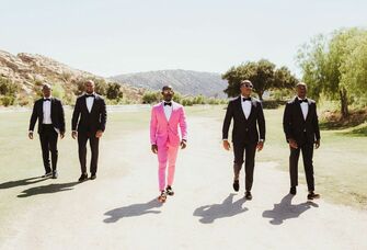 groom & groomsmen in pink and black suits walking near outdoor venue