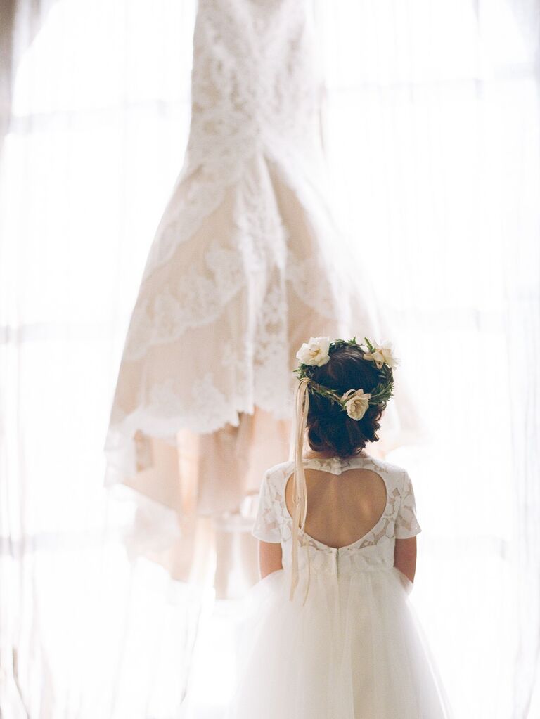 Flower girl gazes at a beautiful white wedding dress. 