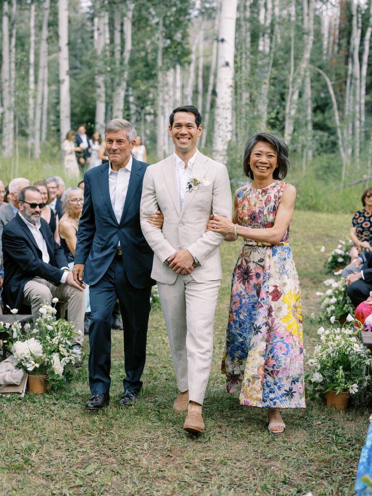Groom in Gray Suit Walking Down Outdoor Ceremony Aisle With Parents