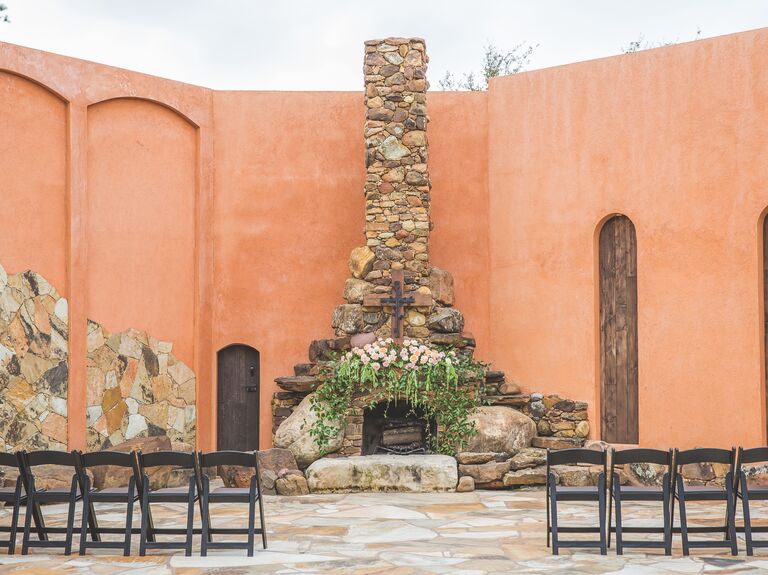 outdoor wedding fireplace made from stones decorated with wooden cross, pink garden roses and greenery vines