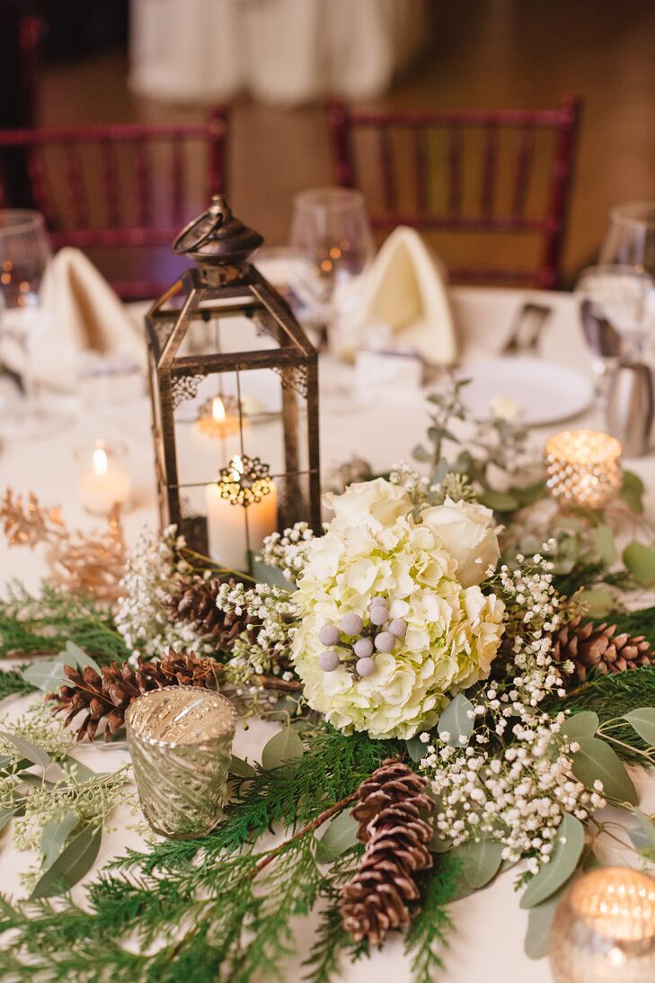 Katie warmed up her winter wedding decor with lanterns and candelabras on every table. The centerpieces also incorporated flowers from her bouquet, like hydrangeas, baby's breath, and pinecones.