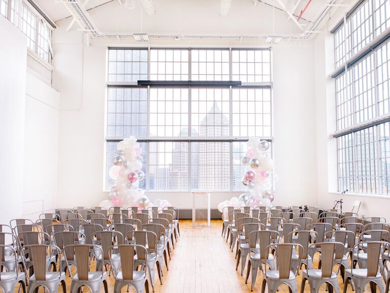 indoor wedding ceremony decorated with white and clear balloon pillars at altar