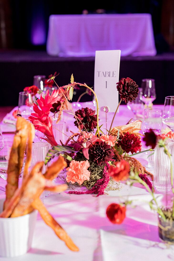 A Low Centerpieces With Colorful Flowers on Crisp White Linen Under Colorful Lighting